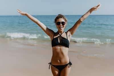 Beautiful young woman having fun on the beach standing with open arms.