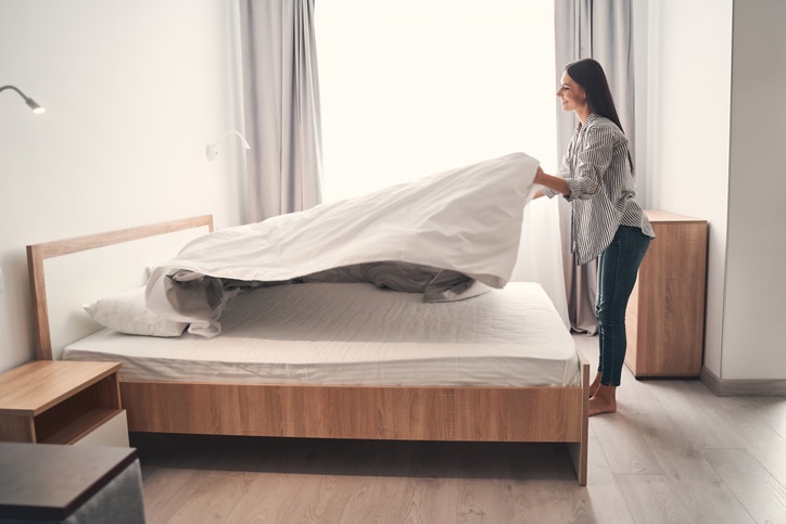 Charming young female person making her bed