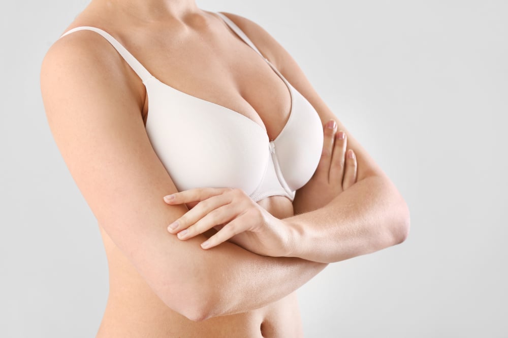 A close-up shot of a woman in a white bra folding her arms over her chest.