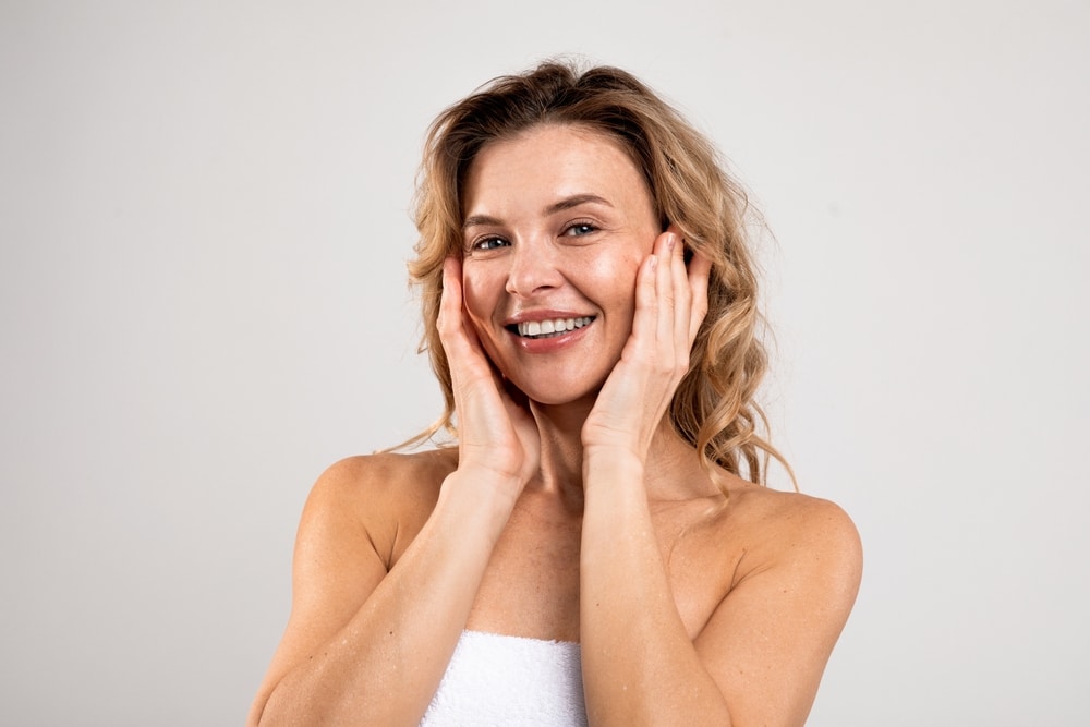 A woman smiling with her hands on her cheeks after cheek augmentation