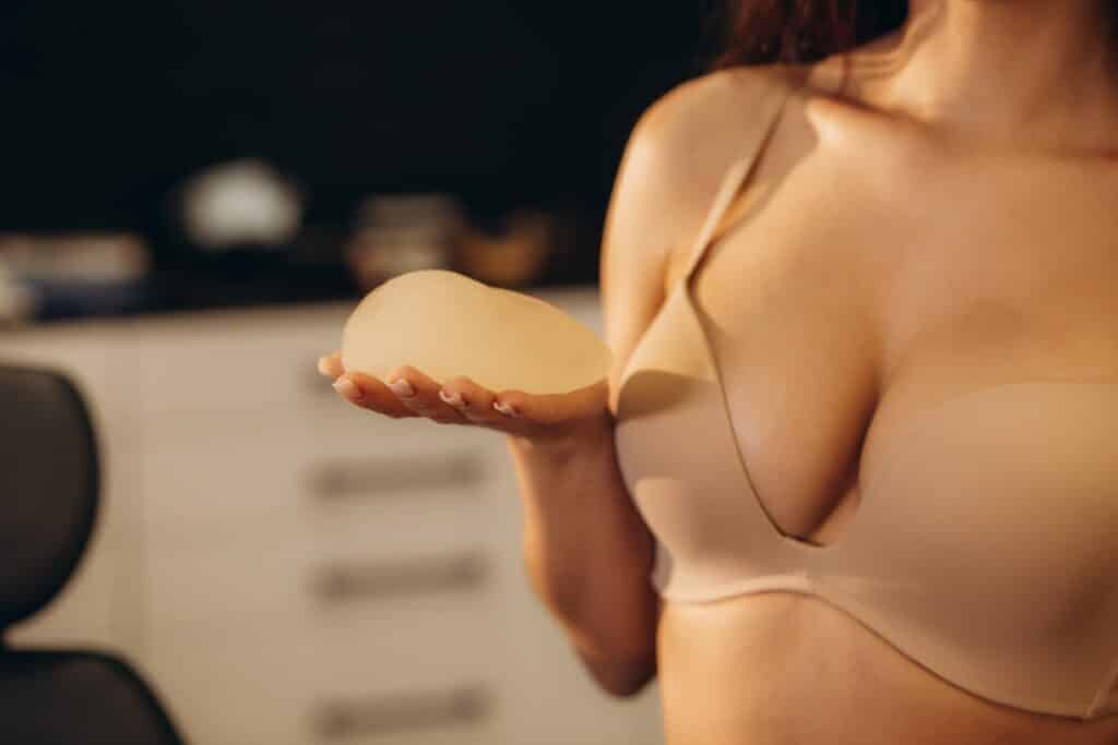 Close up of woman's breasts in bra as she holds breast implant in Huntington Beach, CA